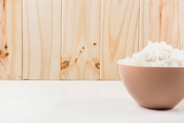 Kom gestoomde rijst op wit bureau tegen houten muur