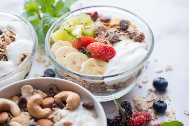 Kom havergranola met yoghurt, verse bosbessen, moerbei, aardbeien, kiwi, banaan, munt en notenbord voor gezond ontbijt, bovenaanzicht, kopieerruimte, plat leggen. vegetarisch voedselconcept.