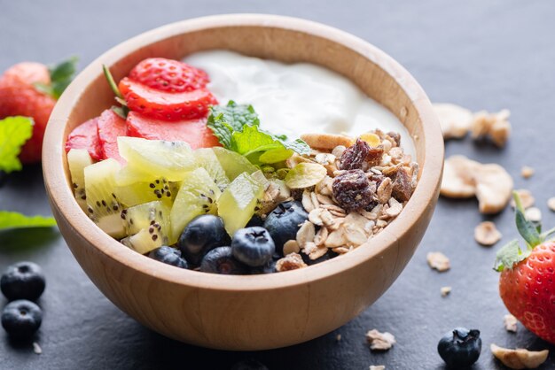 Kom havermuesli met yoghurt, verse bosbessen, aardbeien, kiwimunt en notenbord voor gezond ontbijt, gezond ontbijtmenuconcept. Op de zwarte rots