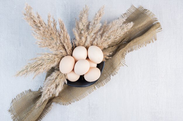 Kom met eieren, een stuk stof en veren grasstengels op marmeren tafel.