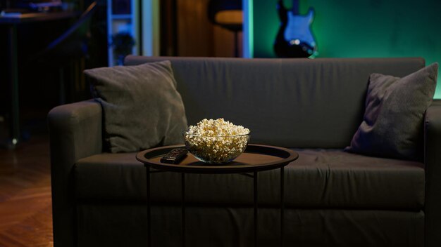 Kom met popcorn op de tafel naast de afstandsbediening in een neonverlicht appartement.