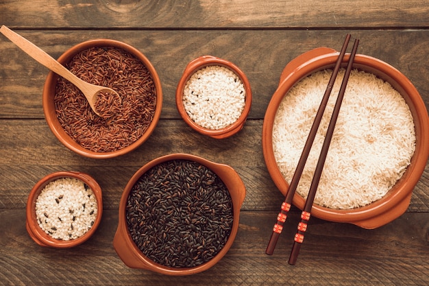 Kom met rood; bruine en witte rijst met houten lepel en eetstokjes