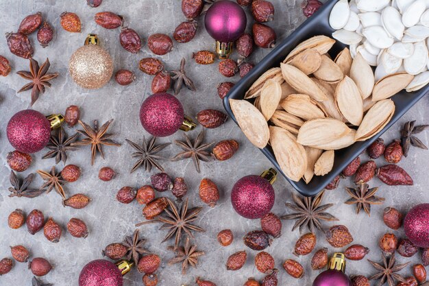 Kom pistache en pompoenpitten met rozenbottels en kerstballen.