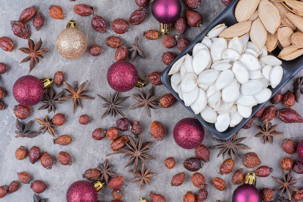 Kom pistache en pompoenpitten met rozenbottels en kerstballen.