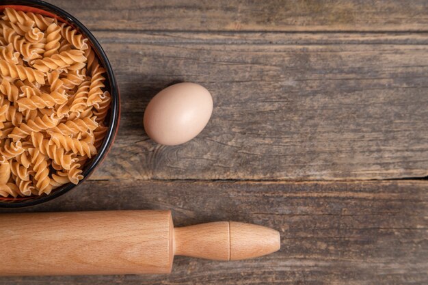 Kom rauwe droge fusilli pasta, deegroller en ei op houten achtergrond. Hoge kwaliteit foto