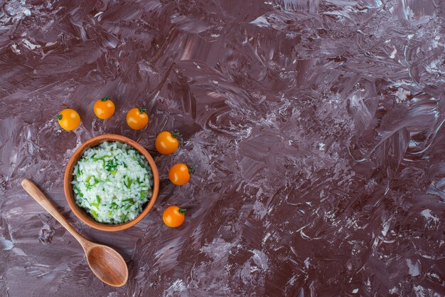 Kom rijst, oranje tomaten en lepel op het marmeren oppervlak