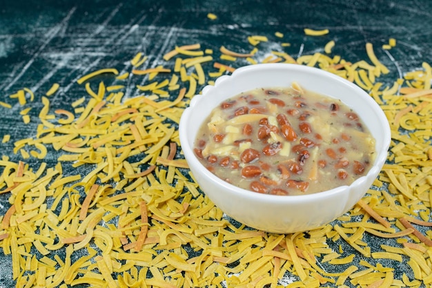 Kom soep met bonen en verspreide pasta op blauwe ruimte.