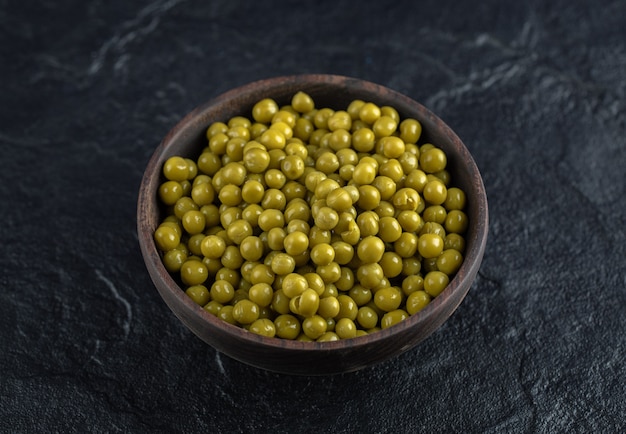 Kom vol met groene gemarineerde groene erwten op zwarte tafel.