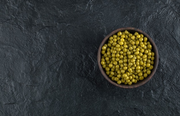 Kom vol met groene gemarineerde groene erwten op zwarte tafel.