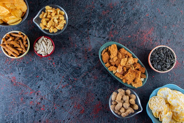 Kommen met knapperige chips, crackers en zonnebloempitten op een donkere ondergrond.