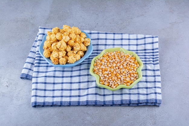 Kommen met maïskorrels en met karamel bedekte popcorn op een handdoek op een marmeren oppervlak