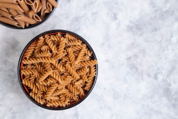 Kommen vol met ongekookte Penne rigate en fusilli-pasta op marmer