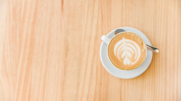 Kop cappuccinokoffie met kunst latte en lepel op houten achtergrond