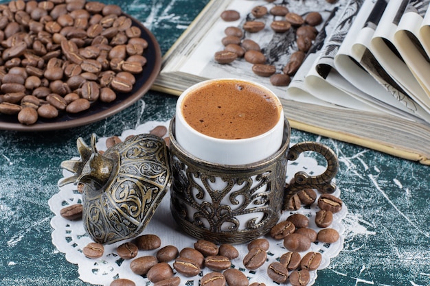 Gratis foto kop schuimende koffie, plaat van koffiebonen en boek over marmeren lijst.