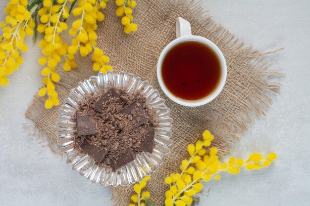 Kop thee en chocoladekom op jute met bloemen. Hoge kwaliteit foto