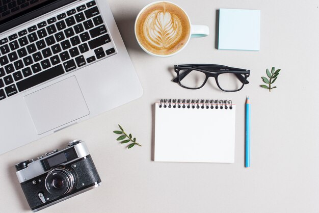 Kop warme koffie cappuccino latte kunst; laptop en camera met stationeries op witte achtergrond