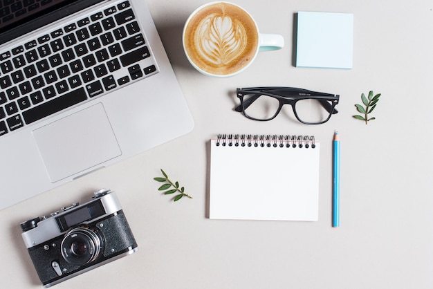 Kop warme koffie cappuccino latte kunst; laptop en camera met stationeries op witte achtergrond