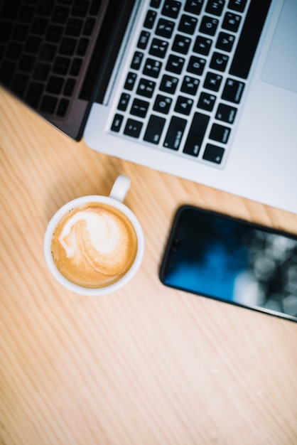 Kopje koffie in de buurt van mobiele telefoon en laptop aan tafel