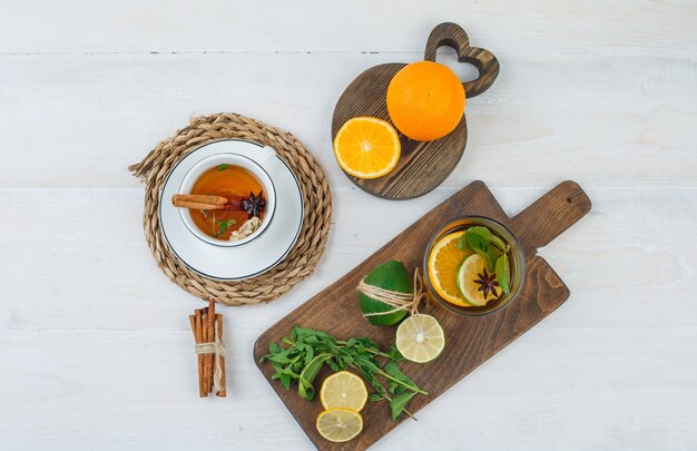 Kopje kruidenthee met citrusvruchten, muntblaadjes op snijplanken en kaneel op witte ondergrond