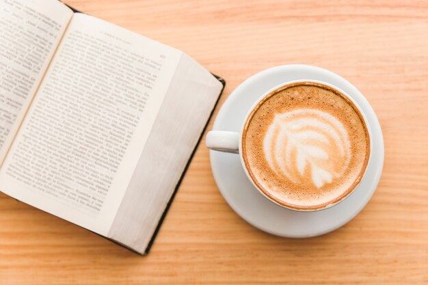 Kopje kunst latte op een cappuccino-koffie en een open boek op tafel