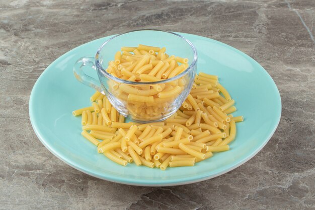 Kopje rauwe macaroni op blauw bord