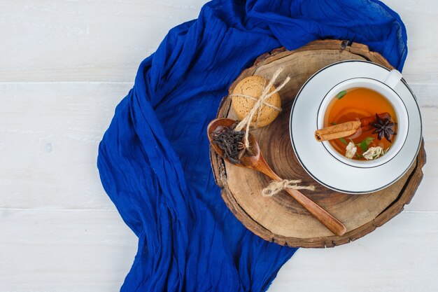 Kopje thee, kruidnagel en koekjes op houten bord met blauwe sjaal