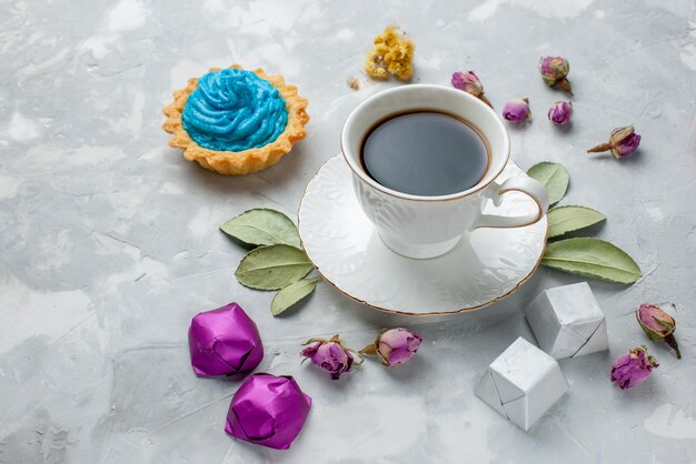 kopje thee met blauwe crème taart chocolade snoepjes op witgrijs bureau, koekje zoet snoep