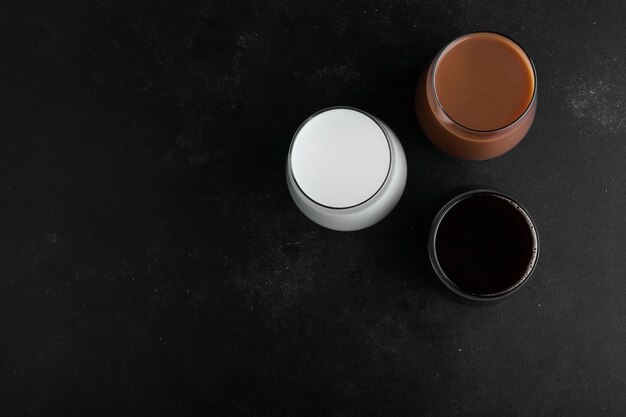 Kopjes melk, chocolade en donkere espresso op zwarte ondergrond, bovenaanzicht.