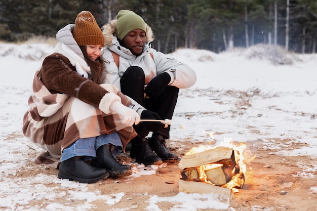 Gratis foto koppel marshmallows roosteren op het vuur tijdens een winterse roadtrip op het strand
