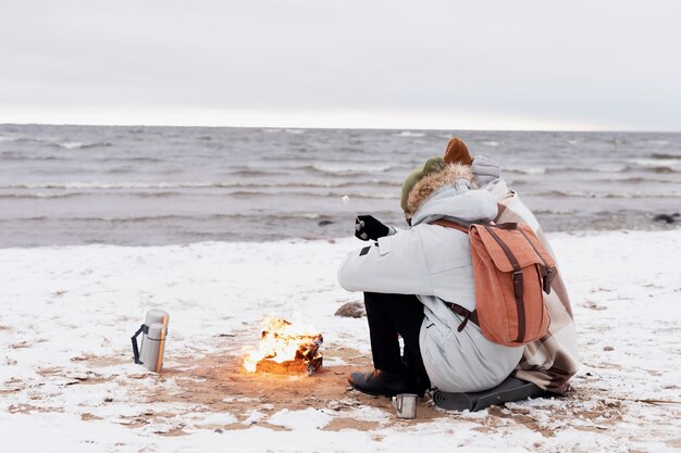 Koppel warmt zich op naast vuur op het strand tijdens een winterse roadtrip