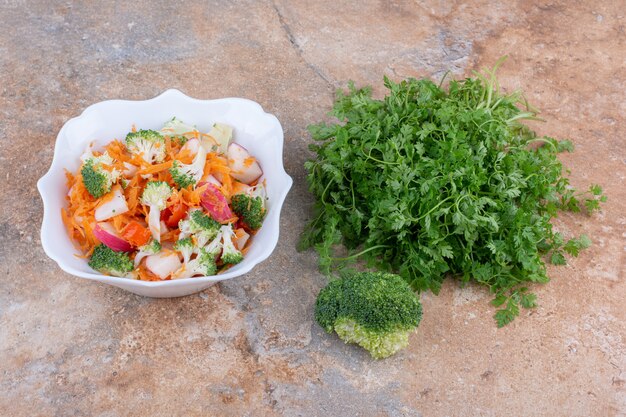 Korianderbundel, broccoli en schotel van gemengde groentesalade die op marmeren oppervlakte wordt getoond