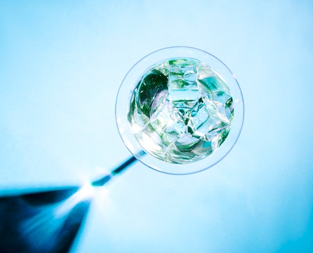 Kristalijsblokjes in het martini-glas met glanzende schaduw op blauwe achtergrond