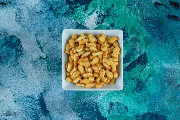 Krokante cracker vis in een kom, op de blauwe tafel.