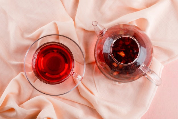 Gratis foto kruiden thee in glazen mok en theepot op roze en textiel.