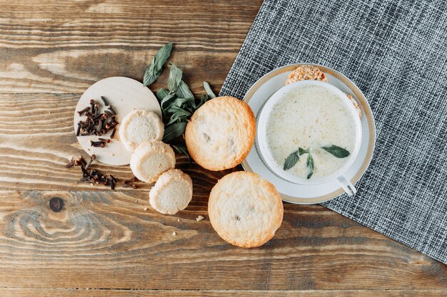 Kruidige melk in een kopje met munt, koekjes, kruidnagel bovenaanzicht op houten tafel