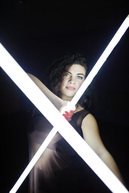 Krullend brunette plus size model met twee lange led-lampen in zwarte kamer