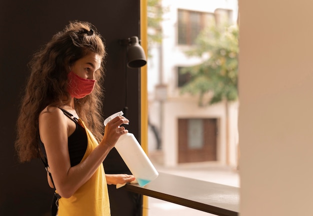 Gratis foto krullende barista die een gezichtsmasker draagt tijdens het schoonmaken in de coffeeshop