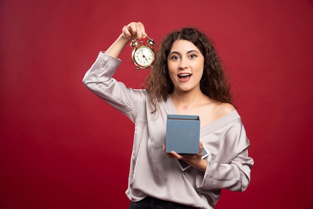 Krullende jonge vrouw die klok uit giftdoos neemt.