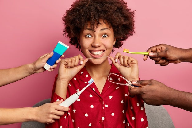 Krullende vrouw geeft om tanden, houdt tandzijde vast, omgeven door tandpasta en borstels