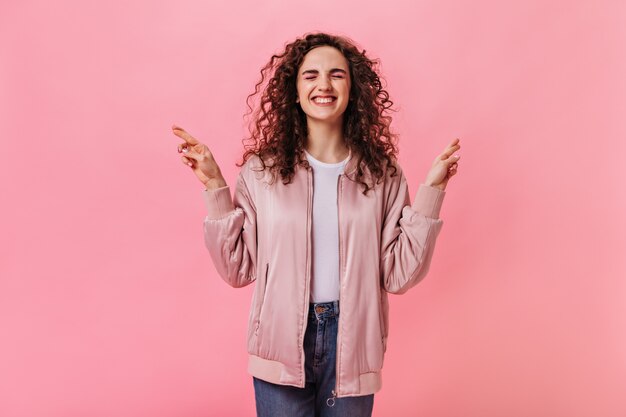 Krullende vrouw in stijlvol jasje gekruiste vingers