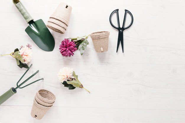 Kunstbloemen; turfpot en tuinieren gereedschappen gerangschikt in cirkelvorm met schaar op witte tafel