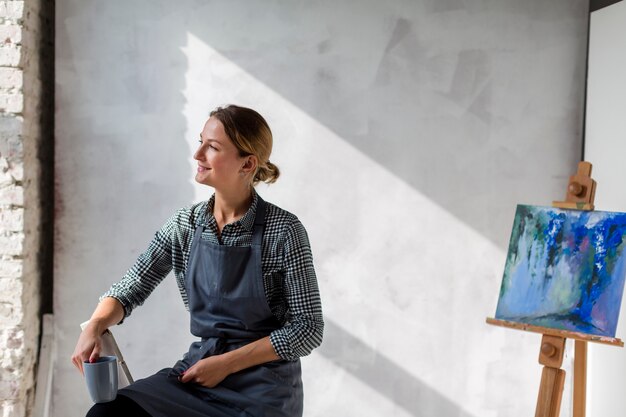 Gratis foto kunstenaarsvrouw het stellen op stoel met schildersezel en het schilderen