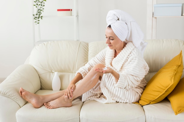 Kuuroord thuis vrouw hydrateert haar benen met body milk long shot