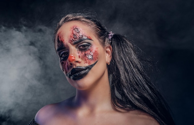 Gratis foto kwaadaardige psycho-clown-make-up ziet er vooral griezelig uit in een rook op een donkere achtergrond.