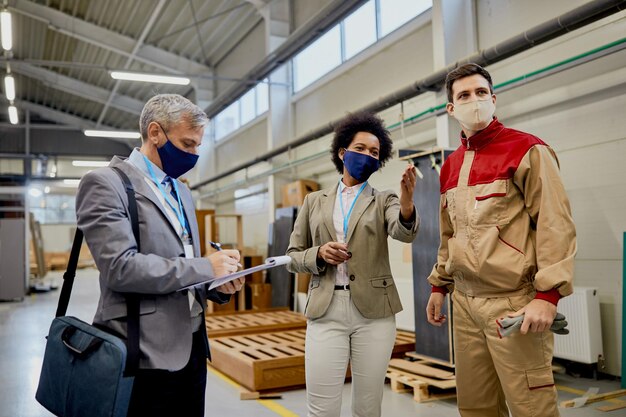 Kwaliteitscontrole-inspecteurs praten met mannelijke werknemer tijdens een bezoek aan een houtbewerkingsfabriek tijdens een pandemie van het coronavirus