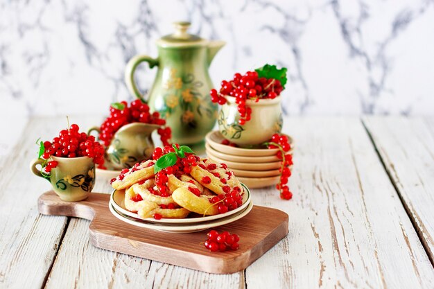 Kwarkkoekjesbroodjes met rode aalbessen op keramische plaat met vintage keramische thee of koffie set, theetijd, ontbijt, zomersnoepjes