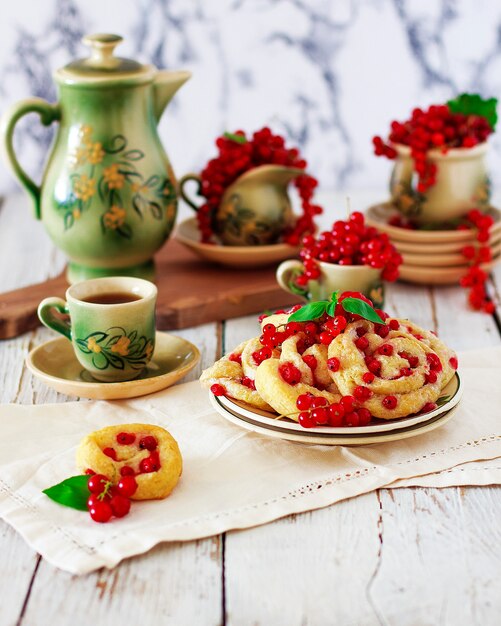 Kwarkkoekjesbroodjes met rode aalbessen op keramische plaat met vintage keramische thee of koffie set, theetijd, ontbijt, zomersnoepjes