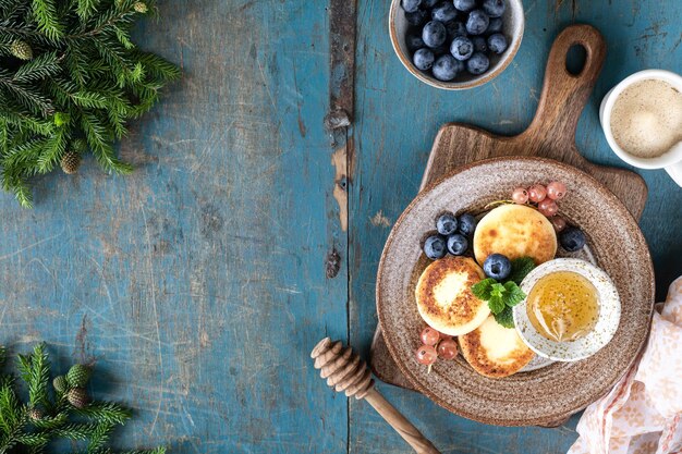 Kwarkpannenkoekjes Kaastaarten met honing, aalbessen en bosbessen op een blauwe achtergrond Zoet voedsel voor het ontbijt voor het nieuwe jaar