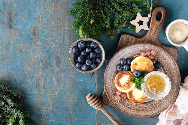 Kwarkpannenkoekjes Kaastaarten met honing, aalbessen en bosbessen op een blauwe achtergrond Zoet voedsel voor het ontbijt voor het nieuwe jaar