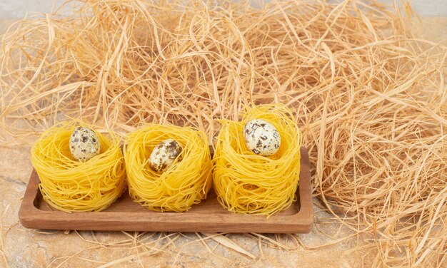 Kwartel ei op een pasta capellini op een bord naast stro, op het marmer.